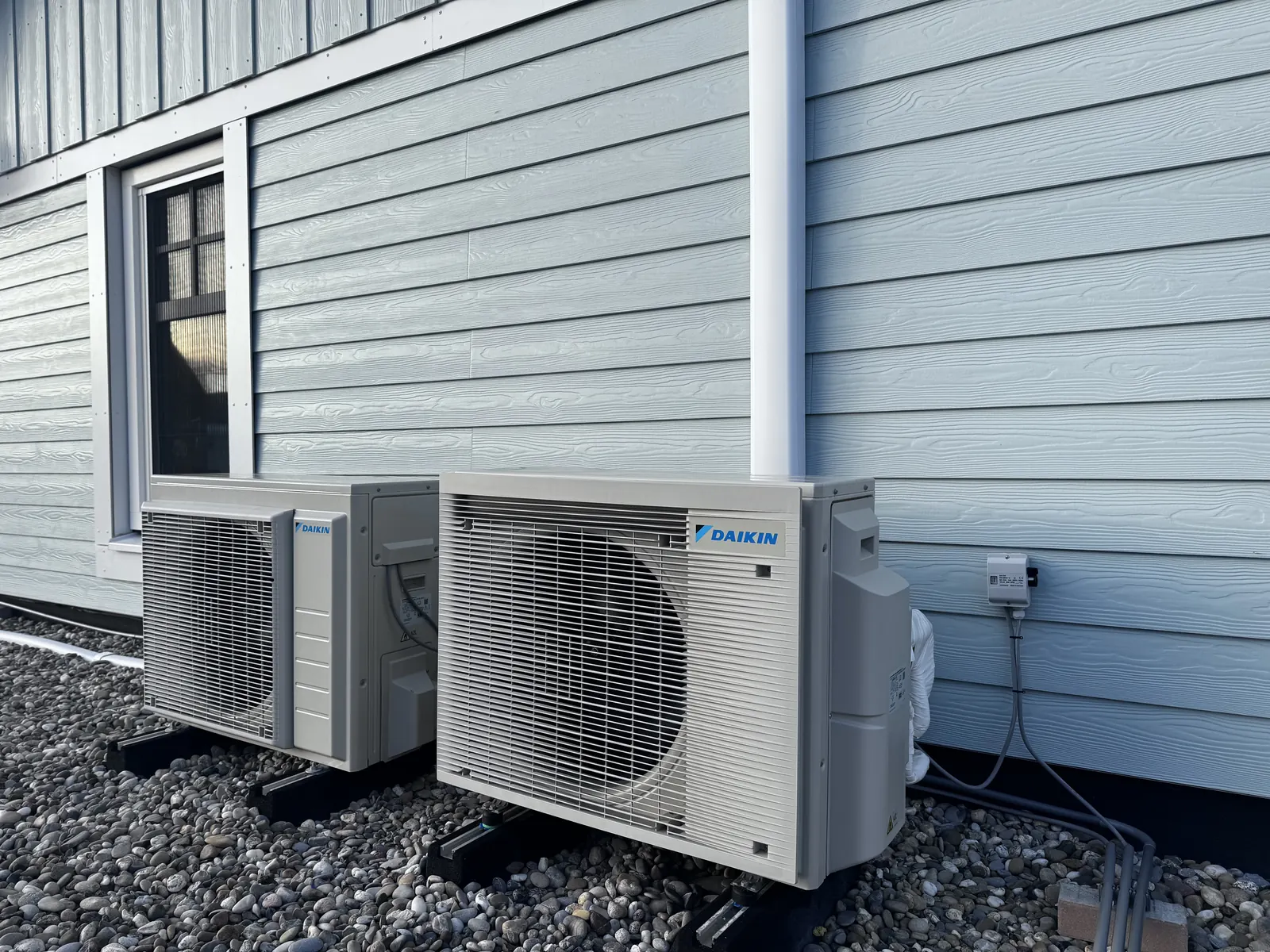 Daikin split-airco aan een blauwe gevel. Daikin split-airco bij een woning met blauwe houten gevel. Leidingen in een koker en units op stelvoeten, door HEAT Nederland.