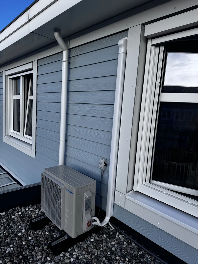 Daikin split-airco aan een blauwe gevel. Daikin split-airco bij een woning met blauwe houten gevel. Leidingen in een koker en units op stelvoeten, door HEAT Nederland.