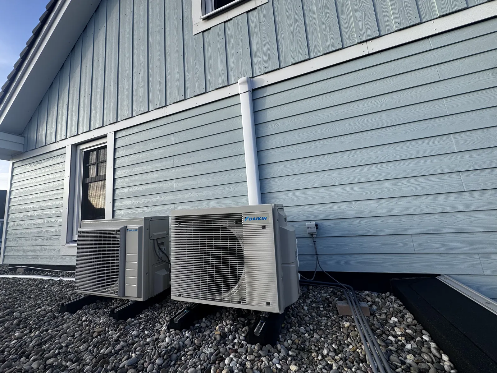 Daikin split-airco aan een blauwe gevel. Daikin split-airco bij een woning met blauwe houten gevel. Leidingen in een koker en units op stelvoeten, door HEAT Nederland.