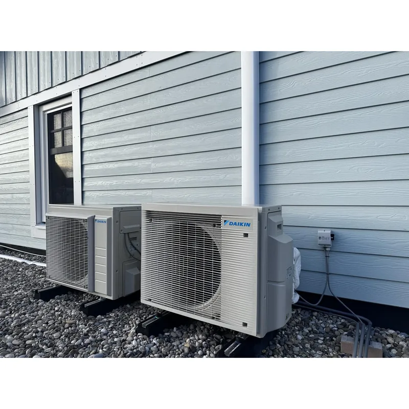 Daikin split-airco aan een blauwe gevel. Daikin split-airco bij een woning met blauwe houten gevel. Leidingen in een koker en units op stelvoeten, door HEAT Nederland.