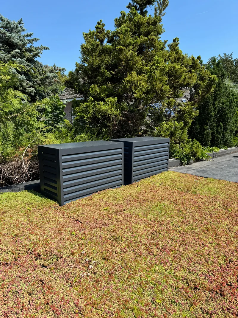Omkasting voor buitenunits op een sedumdak. Twee buitenunits op een sedumdak kregen een antracieten omkasting met open lamellen. Uitgevoerd door HEAT Nederland.