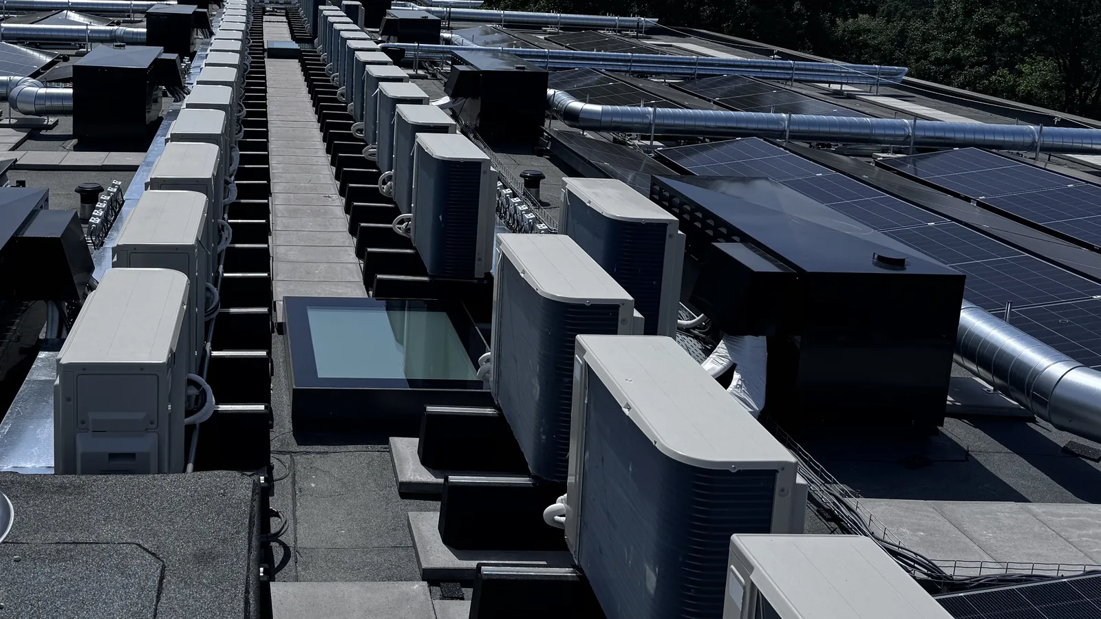 Rij warmtepompunits naast zonnepanelen op een dak